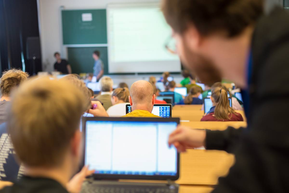 Rear view of students and tutors in a training institute doing practical tasks on their laptops.